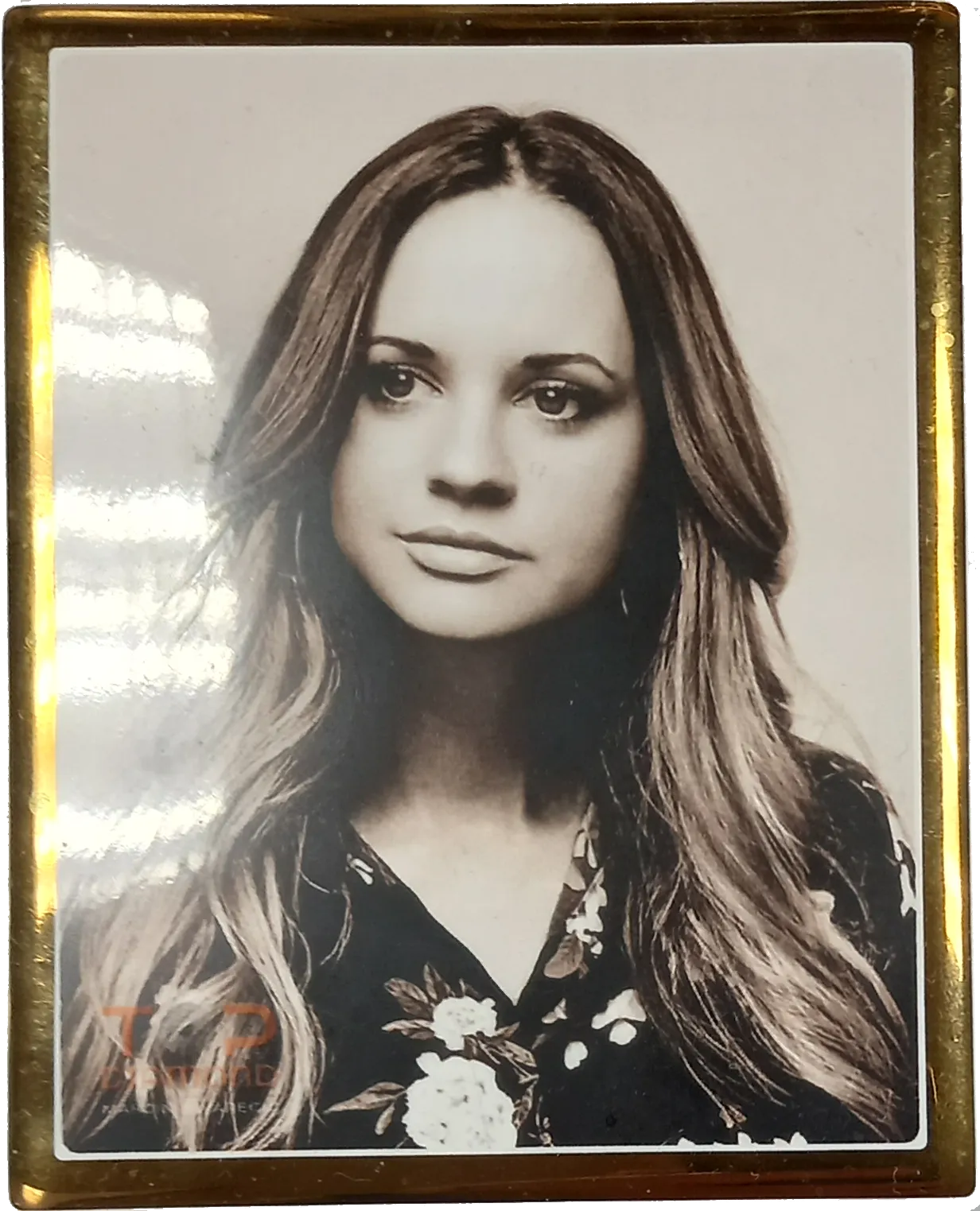 Porcelanowe zdjęcie nagrobkowe, przedstawiające młodą kobietę, oprawione złotą ramką w kształcie prostokąta.